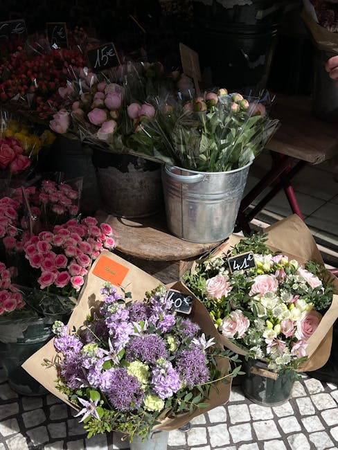 A display of fresh floral arrangements includes three bouquets and a potted plant. The bouquet at the front features purple and lavender flowers, such as alliums and chrysanthemums, wrapped in brown k